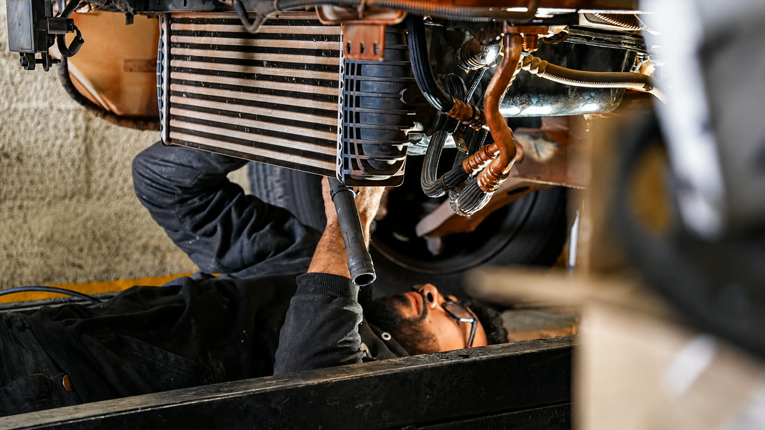 Mecânico da Gueltur deitado sob um veículo, trabalhando na parte inferior do motor