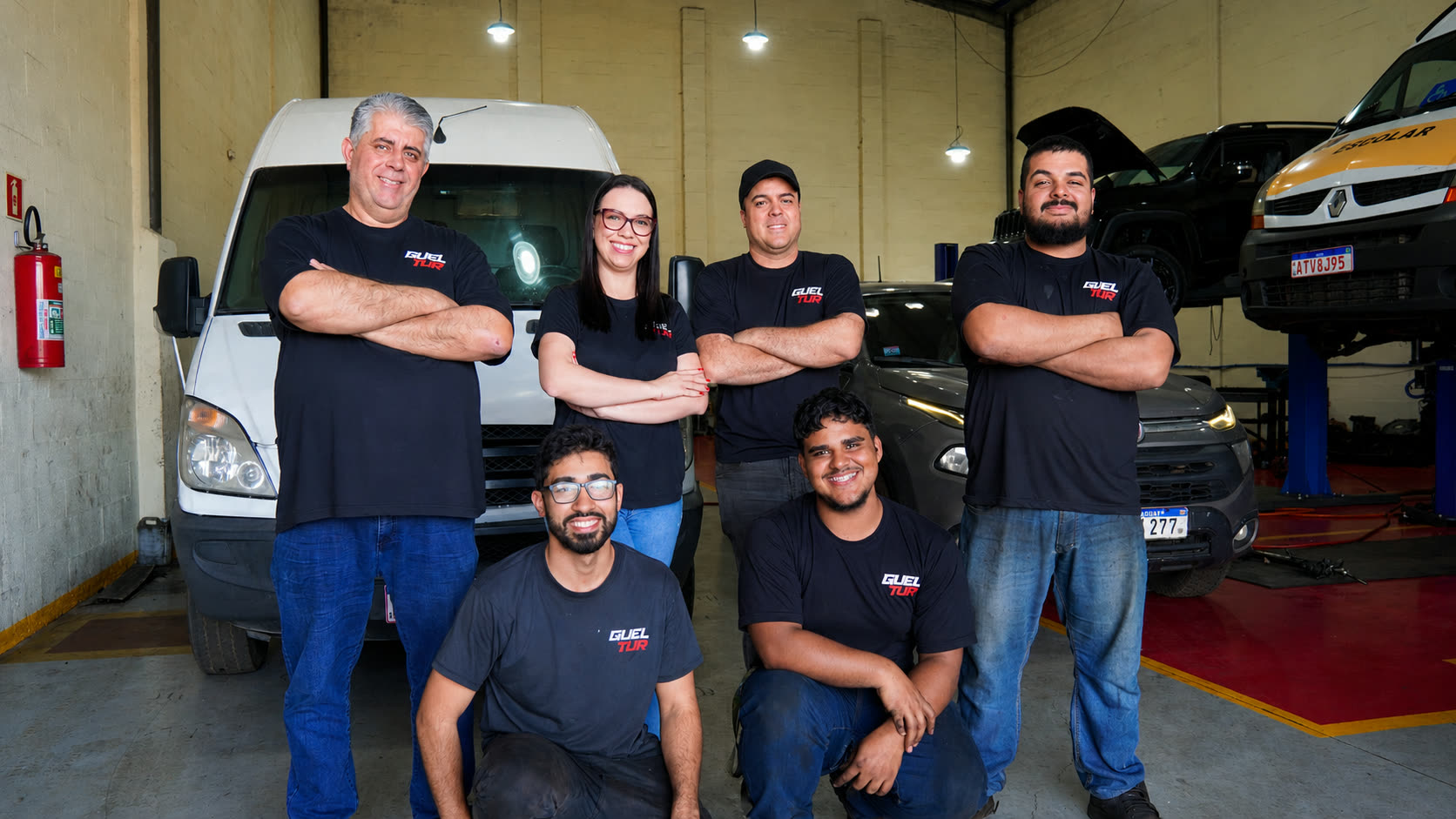 Equipe da Gueltur Diesel reunida na oficina, em frente a uma van e a veículos no elevador